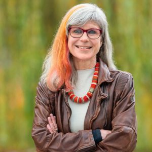 Weibliche Person mit grauen und orangenen Haaren, Brille, Lächeln